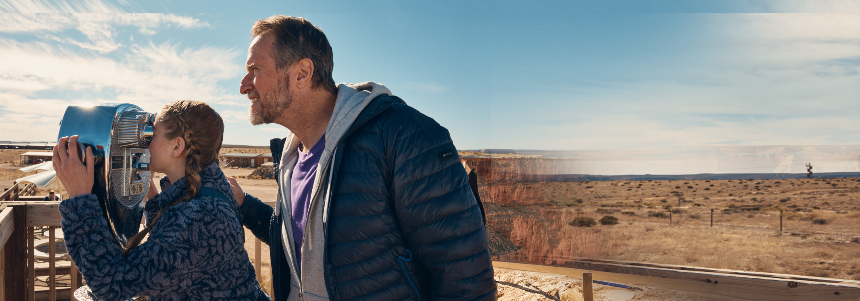 Un padre feliz viendo a su hija usar un telescopio visual.