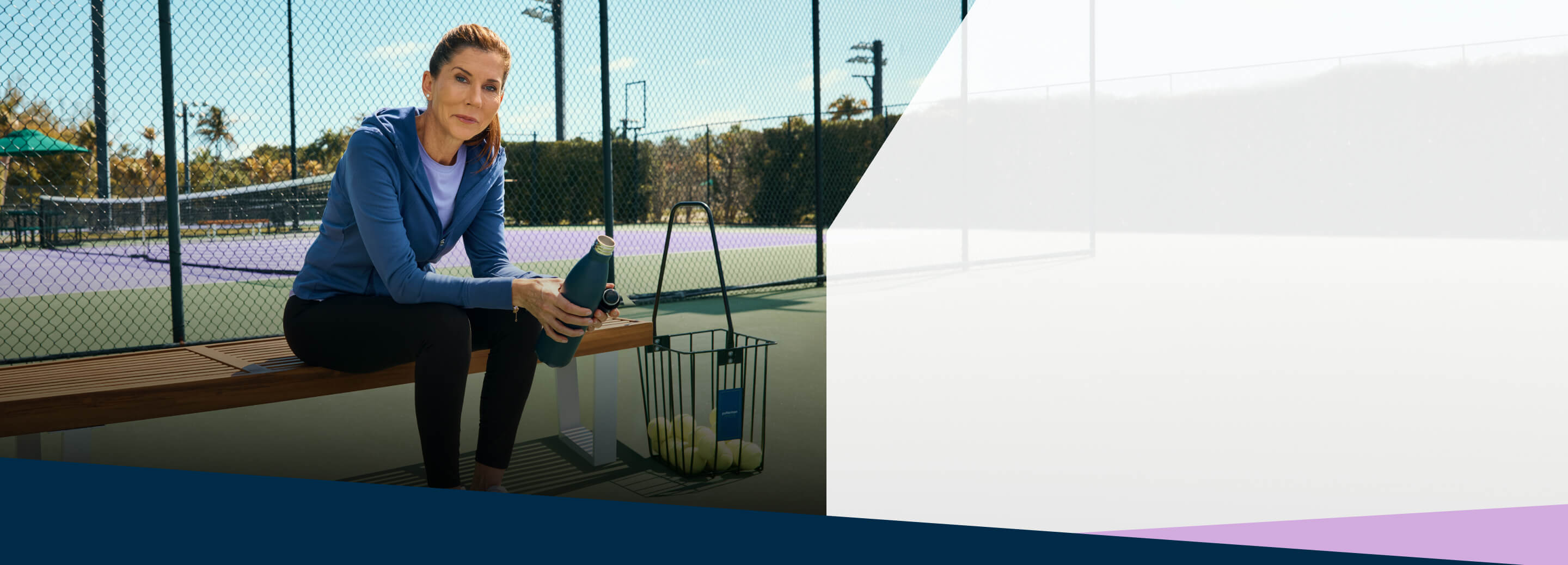 Tennis legend Monica Seles sits on a bench next to a tennis court.