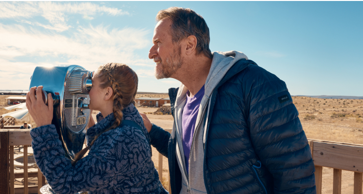 A happy father watching his daughter use a viewing telescope.