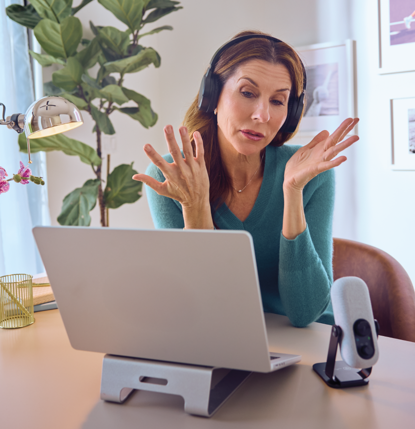 Monica sits at a desk with a laptop and microphone recording a podcast interview.