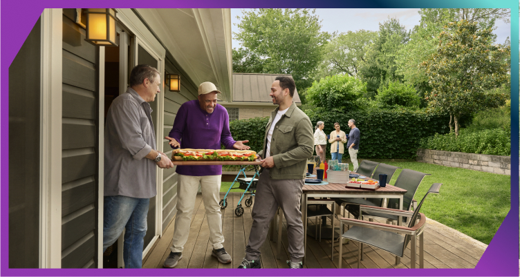 A group of men bringing a large sandwich to a backyard cookout